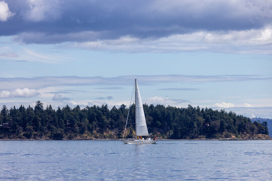 Sailboat Cruising Calm Coastal Waters Near Forested Shoreline Under Dramatic Clouds Off Sidney, Vancouver Island