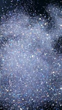 Glitter particles cascade downwards creating a shimmering blue and silver texture in a dark environment.