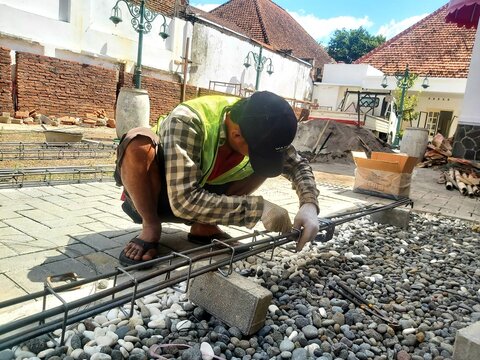 Construction worker assembling and tying rebar column reinforcement at a building construction site before concrete casting.