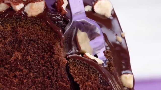 Fork cutting into chocolate cake topped with chocolate glaze and chopped nuts close-up