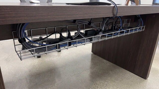 Cable management tray hides a tangle of messy wires and power strips beneath a modern wooden office desk.