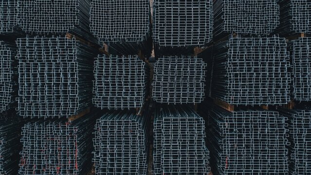 Stacked metal pipes or beams arranged in a grid pattern, viewed from above, with a dark background. Infrastructure and construction materials. Storage and organization of metal components.