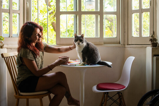 Latina woman petting her cat while having tea