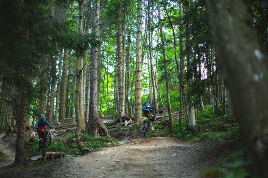 Two mountain bikers riding enduro bikes through a bike park trail,