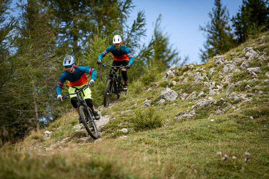 Two mountain bikers riding enduro bikes through a bike park trail,