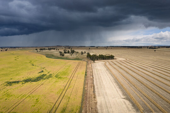 Heavy rain falling from dark clouds over dry harvested farmland