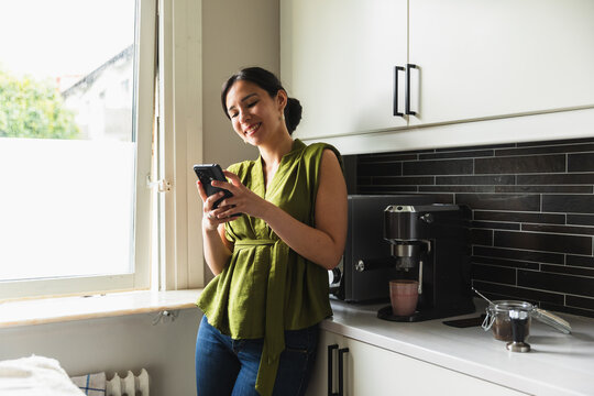 Happy Young Woman Using Smartphone in Kitchen