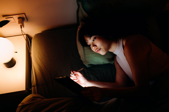 A woman uses a tablet in the bed at night