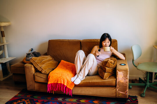 A woman drinks a hot drink sitting on the couch