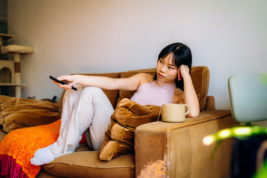 A woman drinks a hot drink sitting on the couch