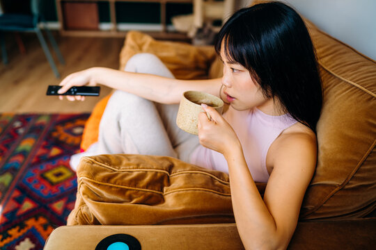 A woman drinks a hot drink sitting on the couch