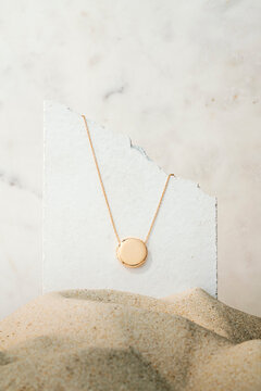 Gold Cİcular Pendant Necklace on Broken White Stone Standing on Sand