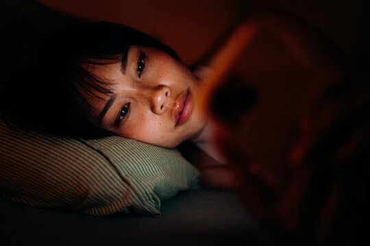 A woman uses a mobile phone in the bed at night