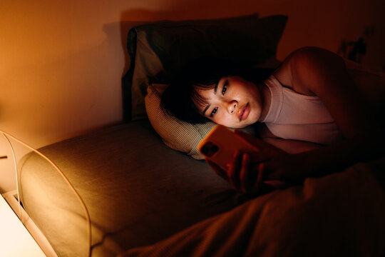 A woman uses a mobile phone in the bed at night