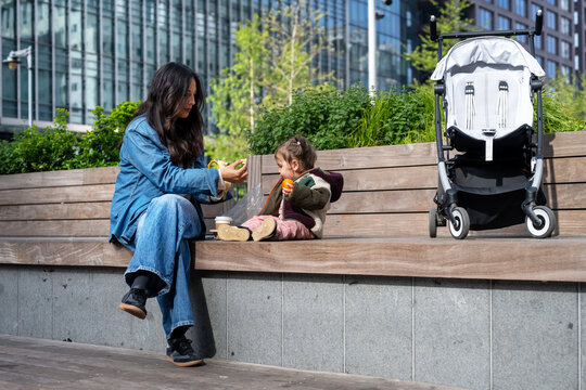 Mother Sharing A Snack With Baby Girl In Urban London Park