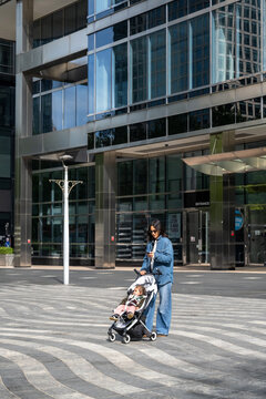 Mother Pushing Baby Girl Through Modern City Plaza In London