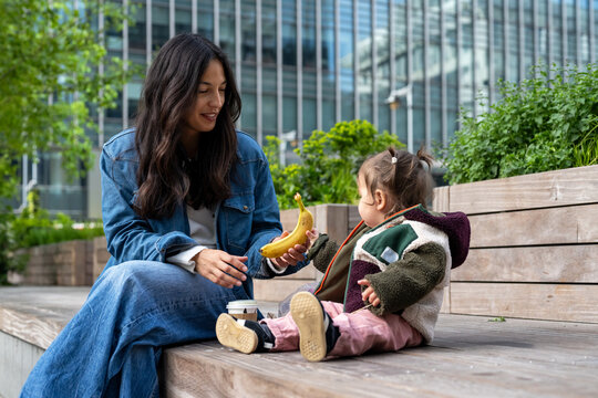 Mother Giving Banana Snack To Baby Girl During A Break In London