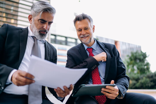 Two businessmen use a tablet outdoors