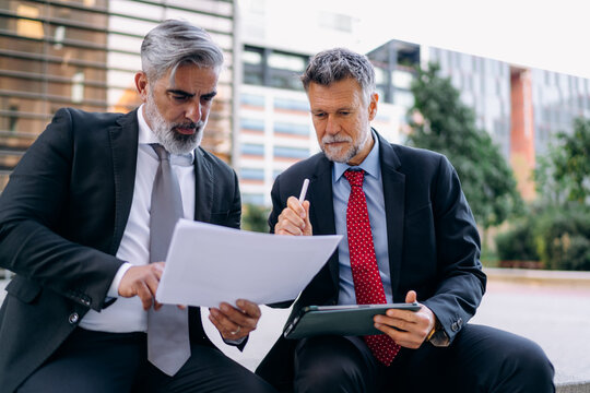 Two businessmen use a tablet outdoors