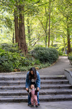 Mother Encouraging Baby Girl During First Steps In London Park