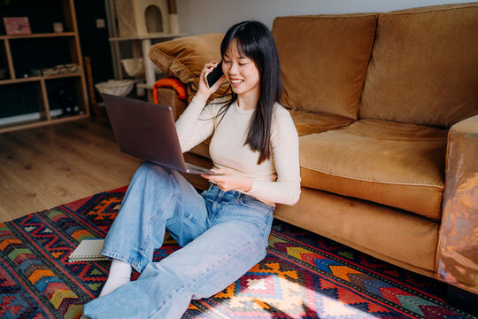 A woman using a mobile phone and laptop at home