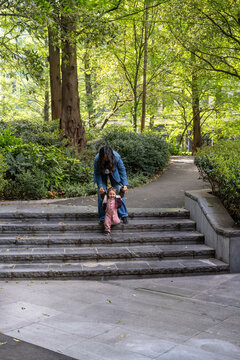 Mother Helping Baby Girl Walk Down Park Step In London