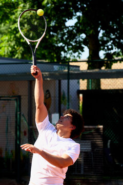 Player Prepares to Serve Tennis Ball on Court Under Sunlight