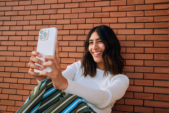 Woman Using Phone by Brick Wall