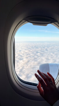A hand rests against a plane window above a cloud layer