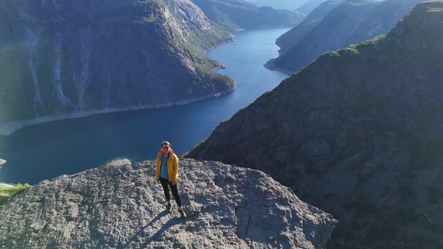 Odda, Norway - 19.07.2026: Drone view of a lone hiker standing on the Trolltunga rock ledge above the blue fjord lake and steep mountains.