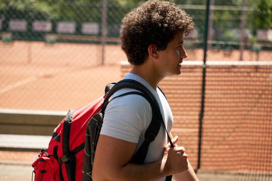 Young Man Arrives With Backpack at Tennis Courts in Sunlight