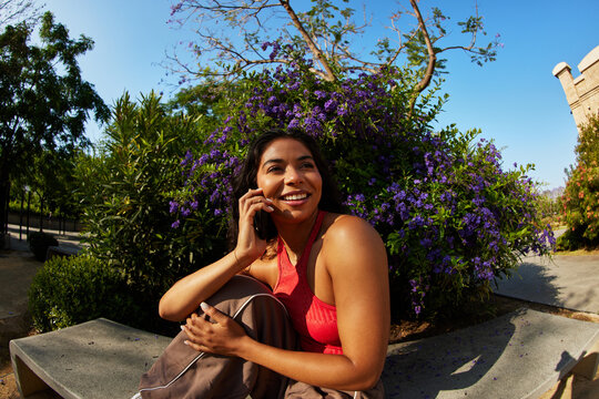 Woman talks on the phone while sitting near flowers in the park