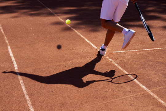 Tennis Player Hits Ball on Clay Court During Warm Sunny Day