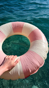 A hand grips a pink striped inflatable ring over clear sea