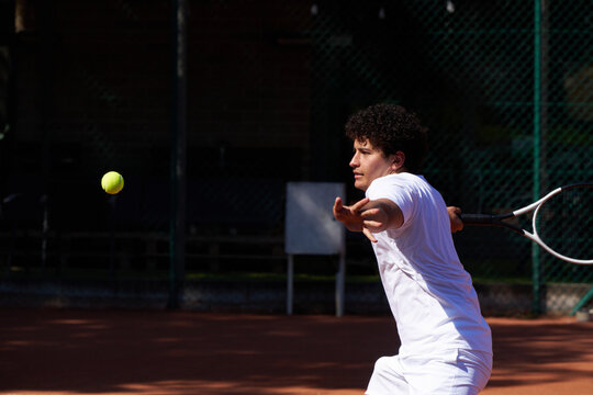 Young Man Plays Tennis on a Court During Sunny Day