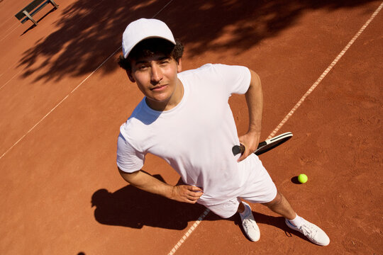 Young Man Practices Tennis on Clay Court During Sunny Day