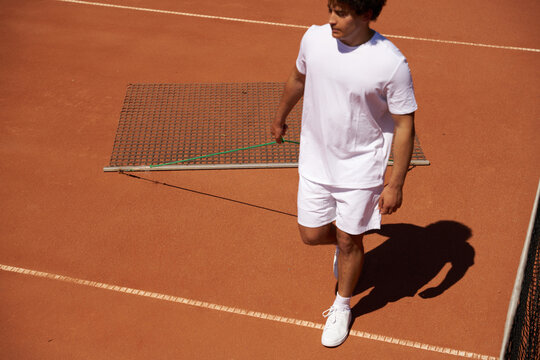 Man Prepares Tennis Court With Equipment in Hand