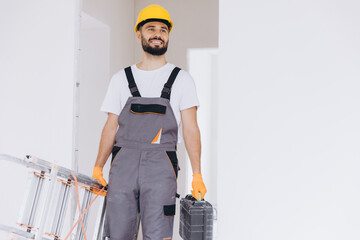Obraz premium Smiling construction worker carrying a ladder and toolbox, ready for home renovation or repair work