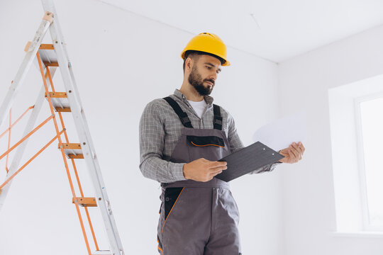 Construction worker checking renovation plans on clipboard, wearing hard hat in a new home interior