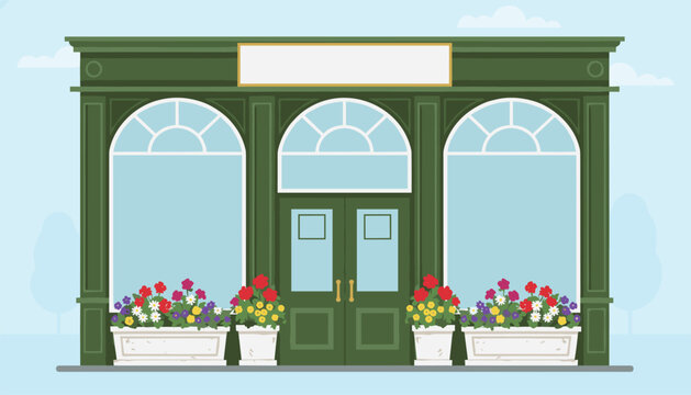 Green vintage storefront exterior with arched windows and potted flower boxes filled with colorful spring blooms.