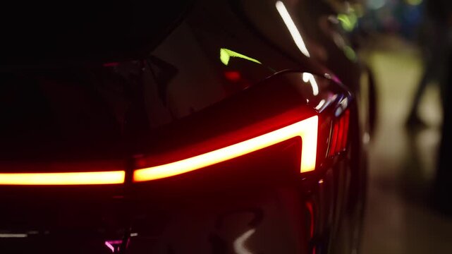 Close-up view of a luxury black electric car's rear red LED light flashing its turn signal, showcasing its futuristic and modern automotive design in a dark setting with reflections
