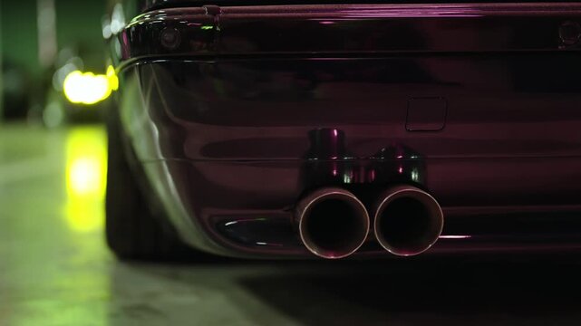 Close-up of a purple sports car's dual exhaust pipes emitting smoke and vapor in a dark garage, highlighting the vehicle's powerful engine and custom tuning for performance racing