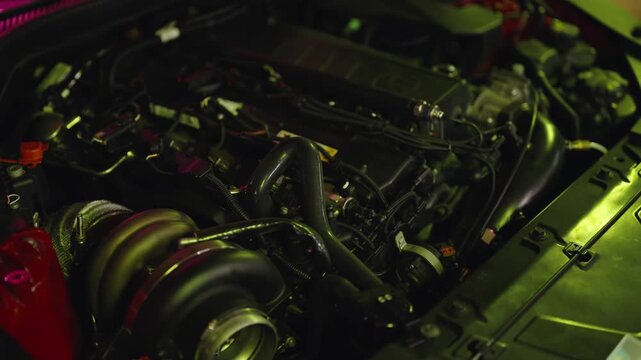 Close-up view of a modified sports car engine with a large turbocharger, detailed parts, and custom modifications under dramatic neon lighting in a mechanic's garage or workshop