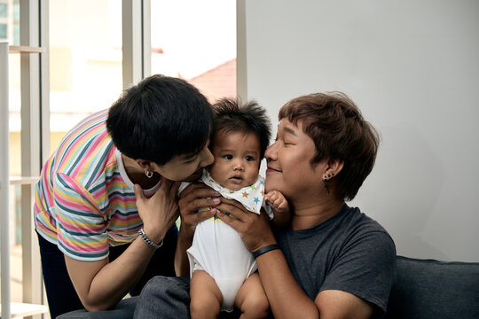 Two men holding and kissing a baby at home, sharing affection, care, bonding, happiness, tenderness, support, comfort, love, and joyful family togetherness