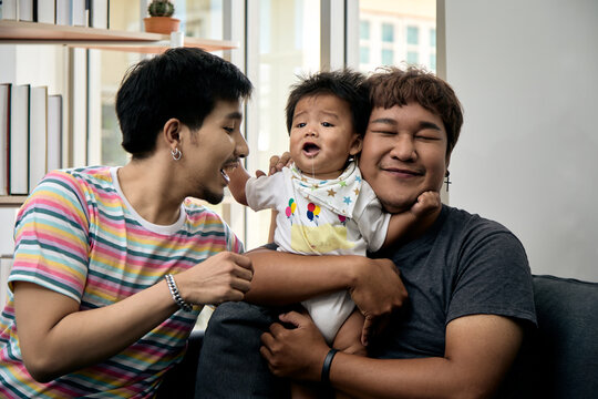 Two men comforting a crying baby on a sofa at home, showing care, affection, support, tenderness, bonding, comfort, concern, caregiving, and emotional family connection