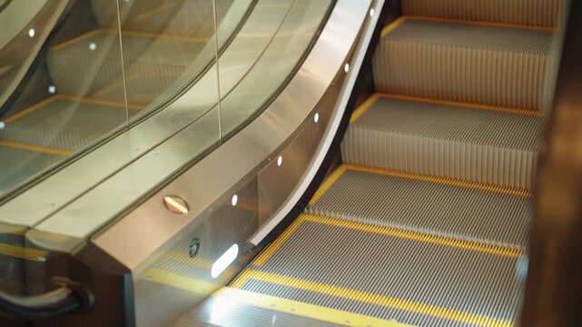 Close-up view of an empty, lit escalator with yellow safety lines automatically moving down in a modern building, showcasing contemporary architectural design and public transportation