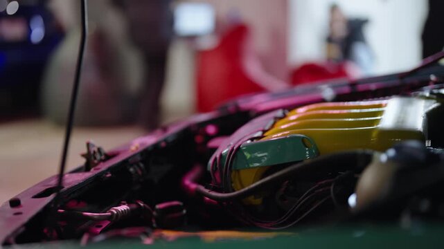 Detailed close-up view of a customized and tuned car engine with an open hood at a motorshow, showcasing modifications and colorful components in a softly lit exhibition environment