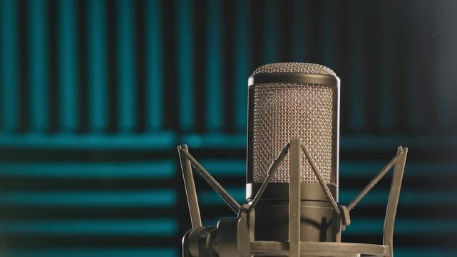 Slow motion colorful studio shot of voiceover dialogue podcast microphone on stand in close-up detail with acoustic foam in recording space with dark background and bright lighting of broadcast vo mic