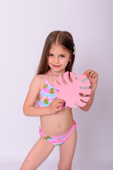 Cute little girl in bright swimwear holding pink tropical paper monstera leaf on white background © Alla