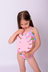 Cute little girl in bright swimwear holding pink tropical paper monstera leaf on white background © Alla
